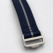 A close-up of a navy blue woven watch strap with a single light silver stripe and a brushed silver metal buckle, shown on a clean white background.