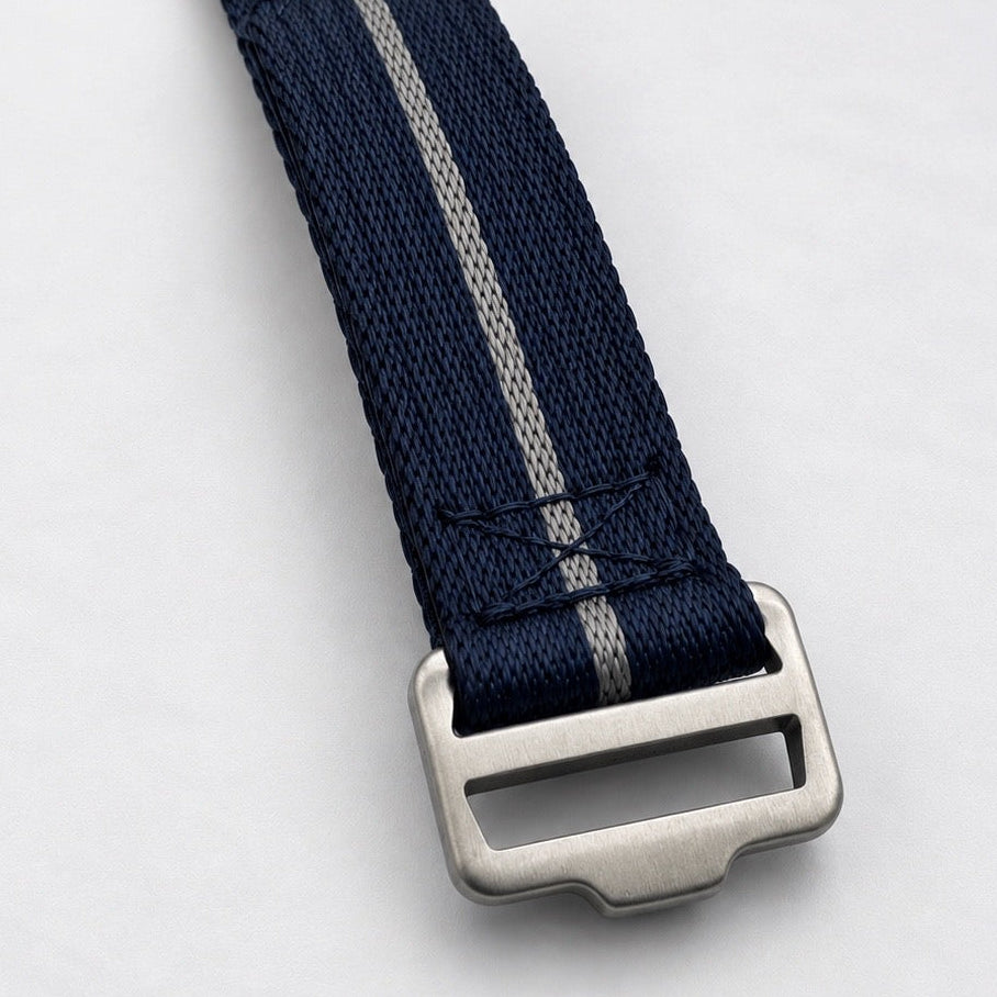 A close-up of a navy blue woven watch strap with a single light silver stripe and a brushed silver metal buckle, shown on a clean white background.